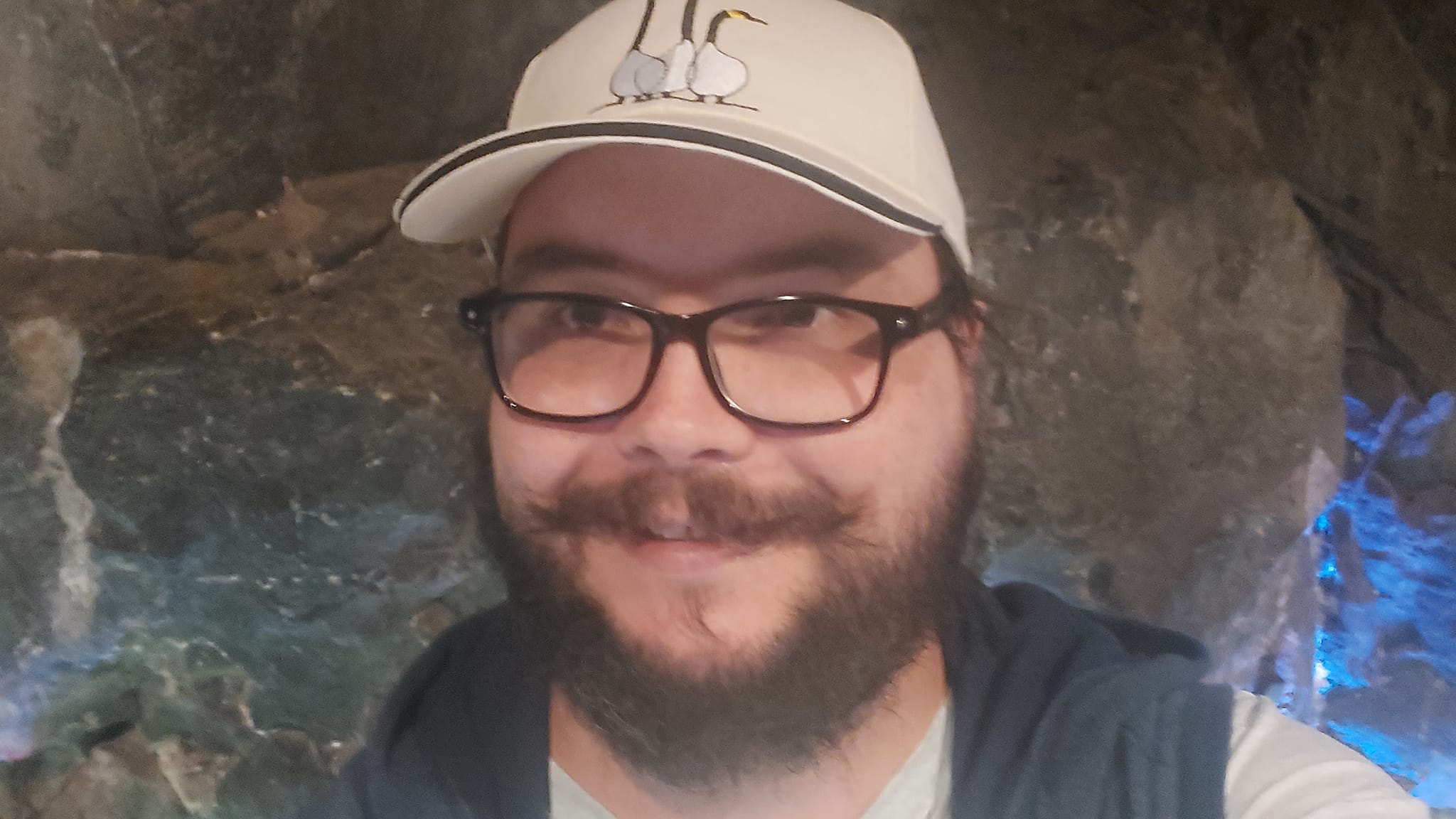 A man with a ball cap and bushy facial hair is standing in front of a solid rock tunnel face